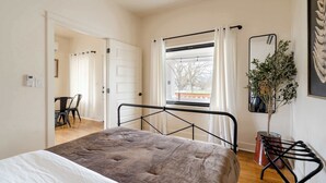 A bedroom with a bed, a window with curtains, a potted plant, and a mirror on the wall. - 1920s Farmhouse | 4BR/2BA | Foodie District (Portland)