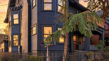 A two-story house with a dark exterior, a visible chimney, and a gated front yard.