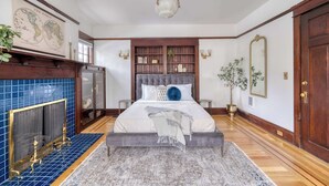 A bedroom with a large bed, a fireplace, a map on the wall, and a wooden bookshelf. - Historic 2BR | Walk to NW 23rd Shops & Eats (Portland)