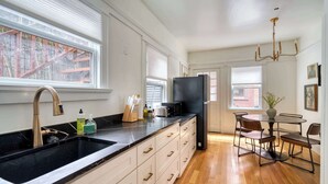 A modern kitchen with a black countertop, white cabinets, and a dining area with a round table and chairs. - Historic 2BR | Walk to NW 23rd Shops & Eats (Portland)