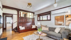 A spacious living room with hardwood floors, a grey sofa, a wooden bench, and a round coffee table. - Historic 2BR | Walk to NW 23rd Shops & Eats (Portland)