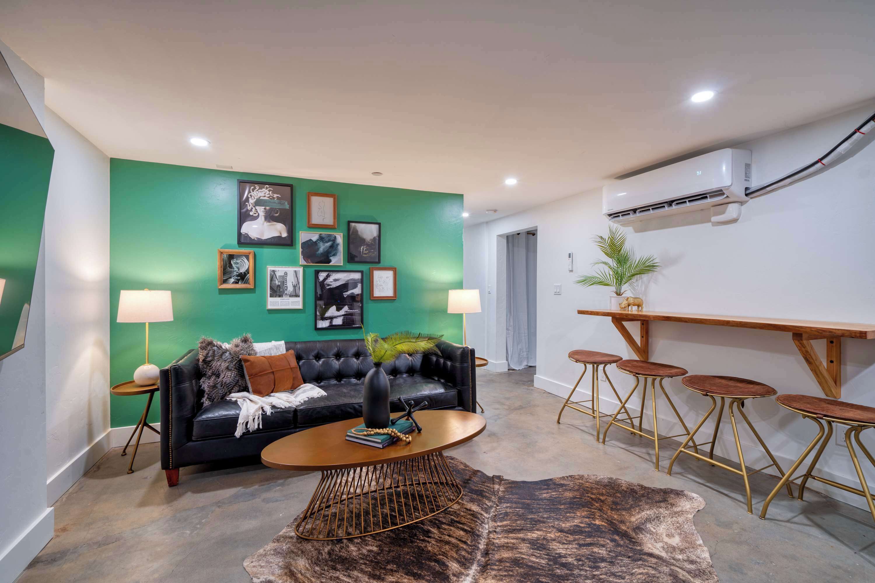 Uma sala de estar moderna com uma parede verde de destaque, um sofá de couro preto, uma mesa de centro redonda e uma área de jantar com banquetas.
