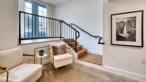 Eine Treppe mit schwarzer Geländer, eine weiße Wand mit einem gerahmten Bild und ein beiges Sofa mit einer kleinen Pflanze.