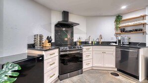 A modern kitchen with a built-in oven, a stove, and a black range hood. There are white cabinets with gold handles, a black countertop, and a plant on the left. - Historic Nob Hill 2BR | Prime Walkable Spot (Portland)