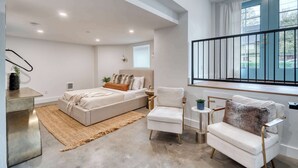 Ein modernes Schlafzimmer mit einem Bett, zwei Stühlen, einem kleinen Tisch und einem Fenster mit Blick.