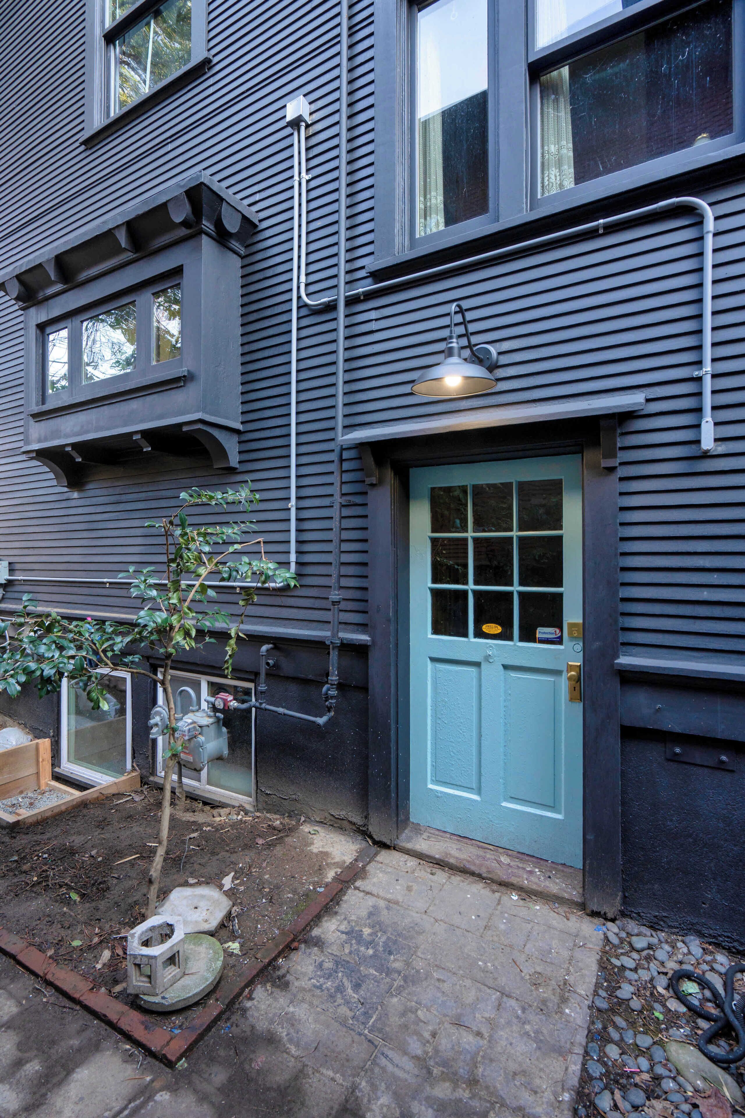 A house with a blue door, a small tree, and a hose on the ground.