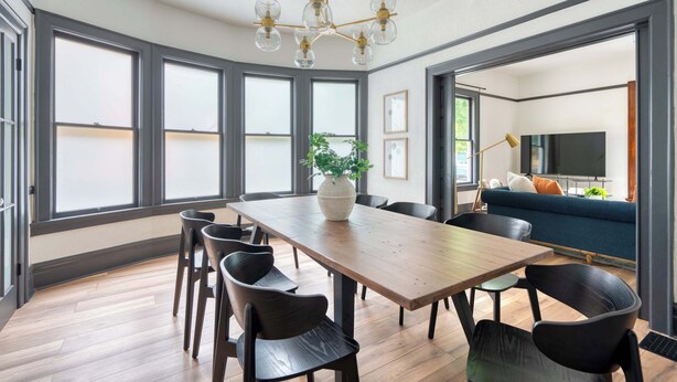 A spacious dining area with a wooden table and black chairs, a chandelier, and large windows. - Luxury Living on NW 23rd Ave, Walk Score 99 (Portland)