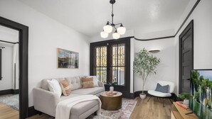 A modern living room with a sofa, coffee table, and a TV. There is a large window with a view of trees and a door with a black frame. - Luxury Living on NW 23rd Ave, Walk Score 99 (Portland)