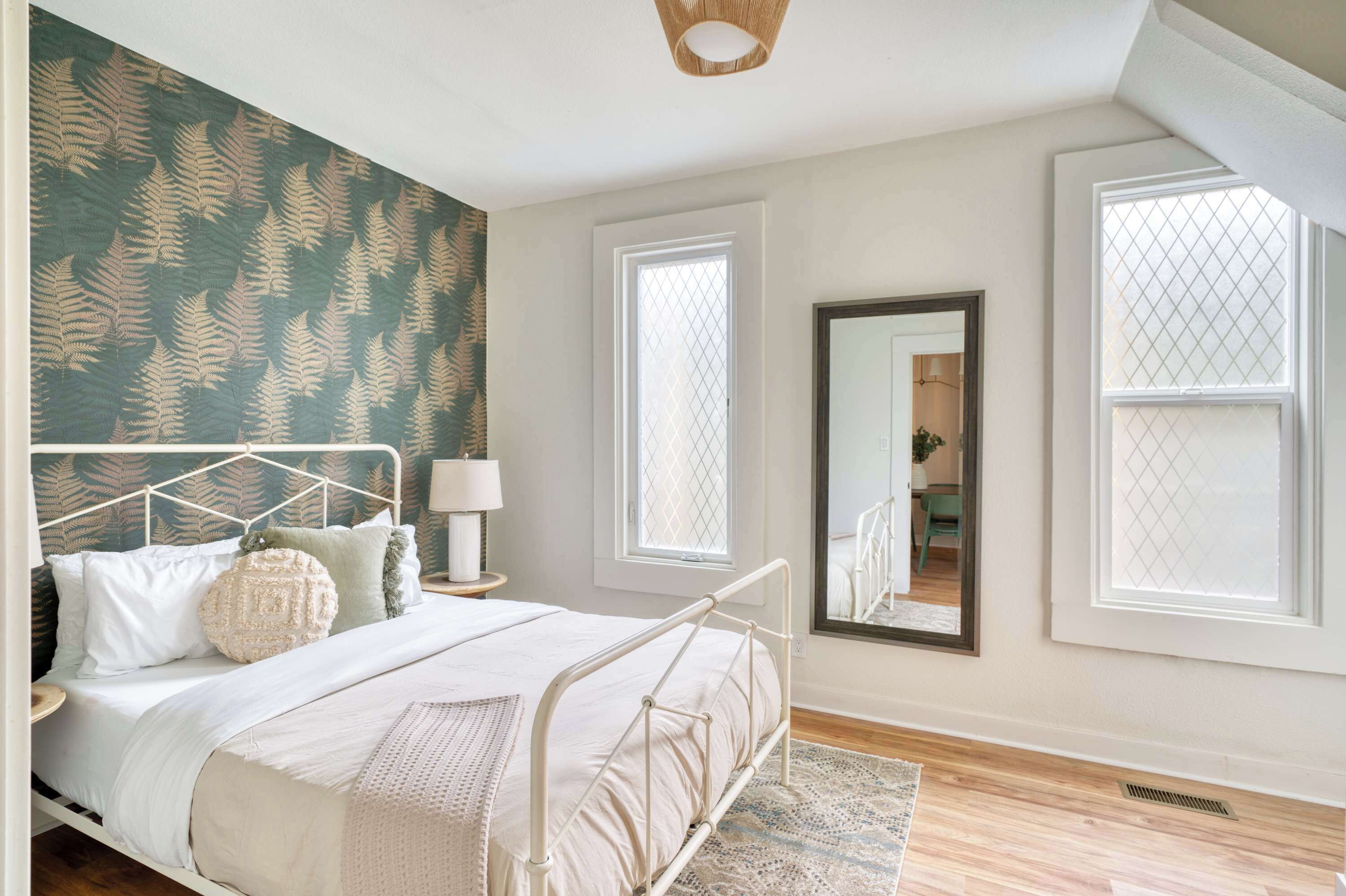 A bedroom with a bed, a nightstand, a mirror, and two windows.