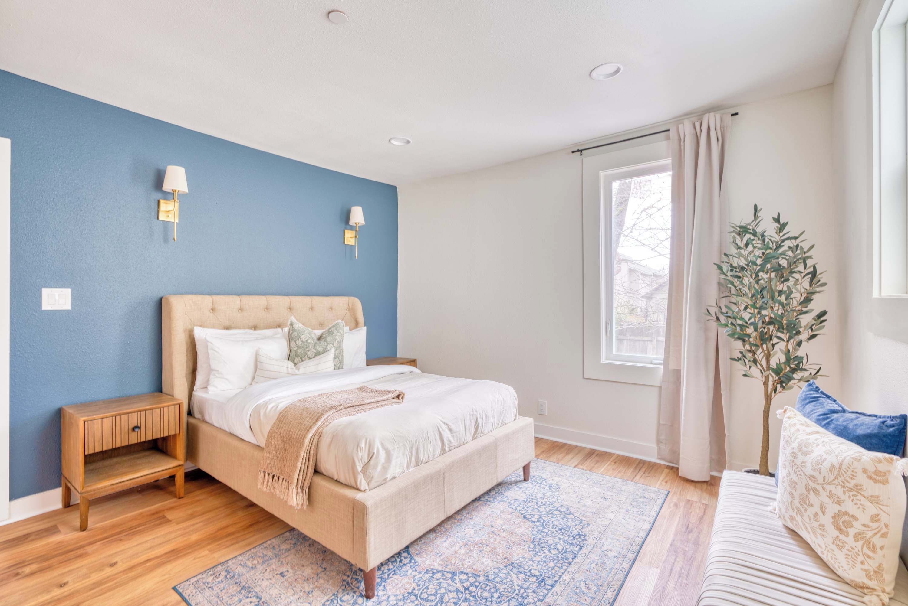 A bedroom with a bed, bedside tables, a window with curtains, and a potted plant.