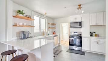 A modern kitchen with white cabinetry, a central island with stools, a microwave, oven, and a sink.