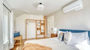 A bedroom with a bed, a bedside table, a lamp, a wardrobe, and an air conditioning unit.