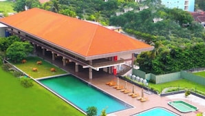 Un hotel con una amplia piscina, zona de estar al aire libre techada y abundante vegetación.