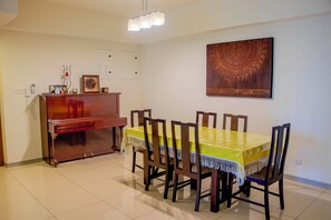 Un coin repas avec un piano en bois, une table recouverte d’une nappe jaune et six chaises.