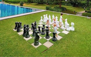 Un jeu d’échecs installé sur une pelouse, avec une piscine en arrière-plan.