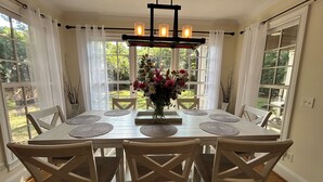 A dining area with a white table, six chairs, a chandelier, and a vase of flowers.