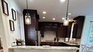 A modern kitchen with dark wood cabinets, a central island with bar stools, and pendant lighting.