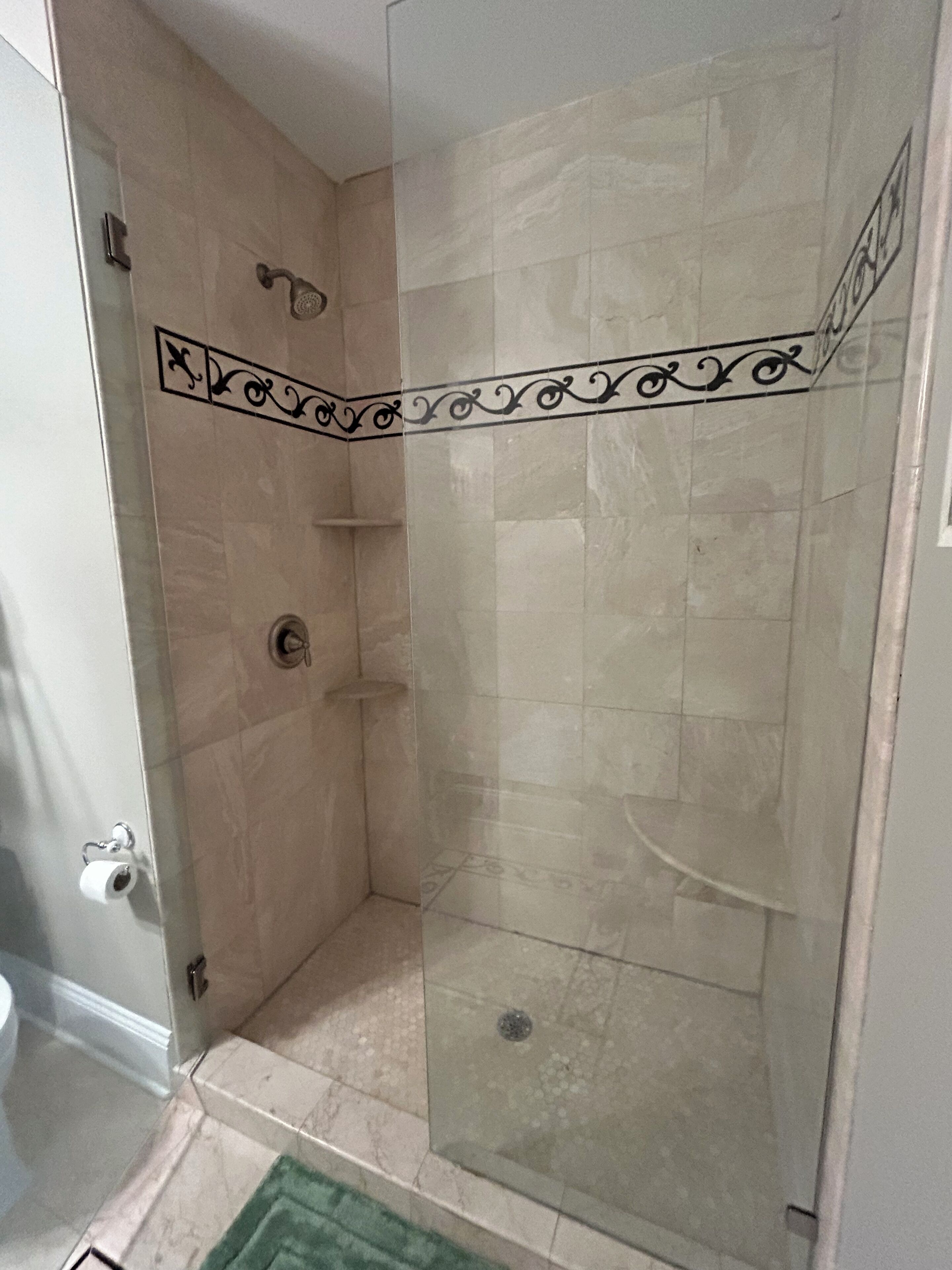 A glass-enclosed shower with beige tiles and a decorative border.