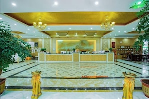 Un hall d’hôtel comprenant un comptoir d’accueil, un espace salon et des plantes décoratives.