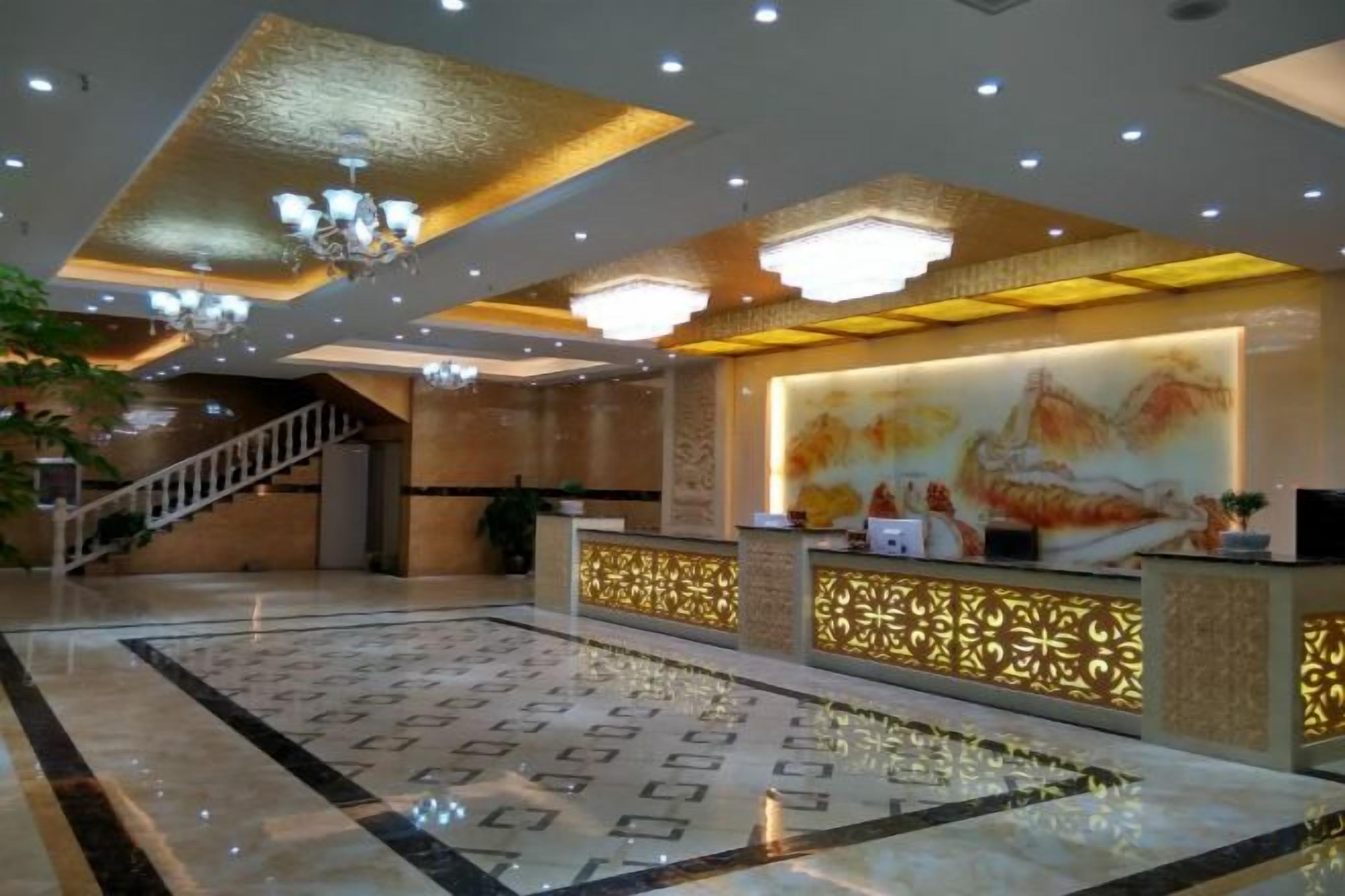 A hotel lobby with a reception desk, a patterned floor, and a staircase.