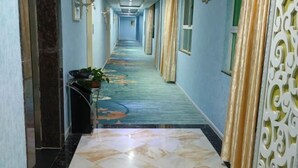 Un corridoio d'hotel con una moquette a fantasia, un pavimento piastrellato e tende decorative.