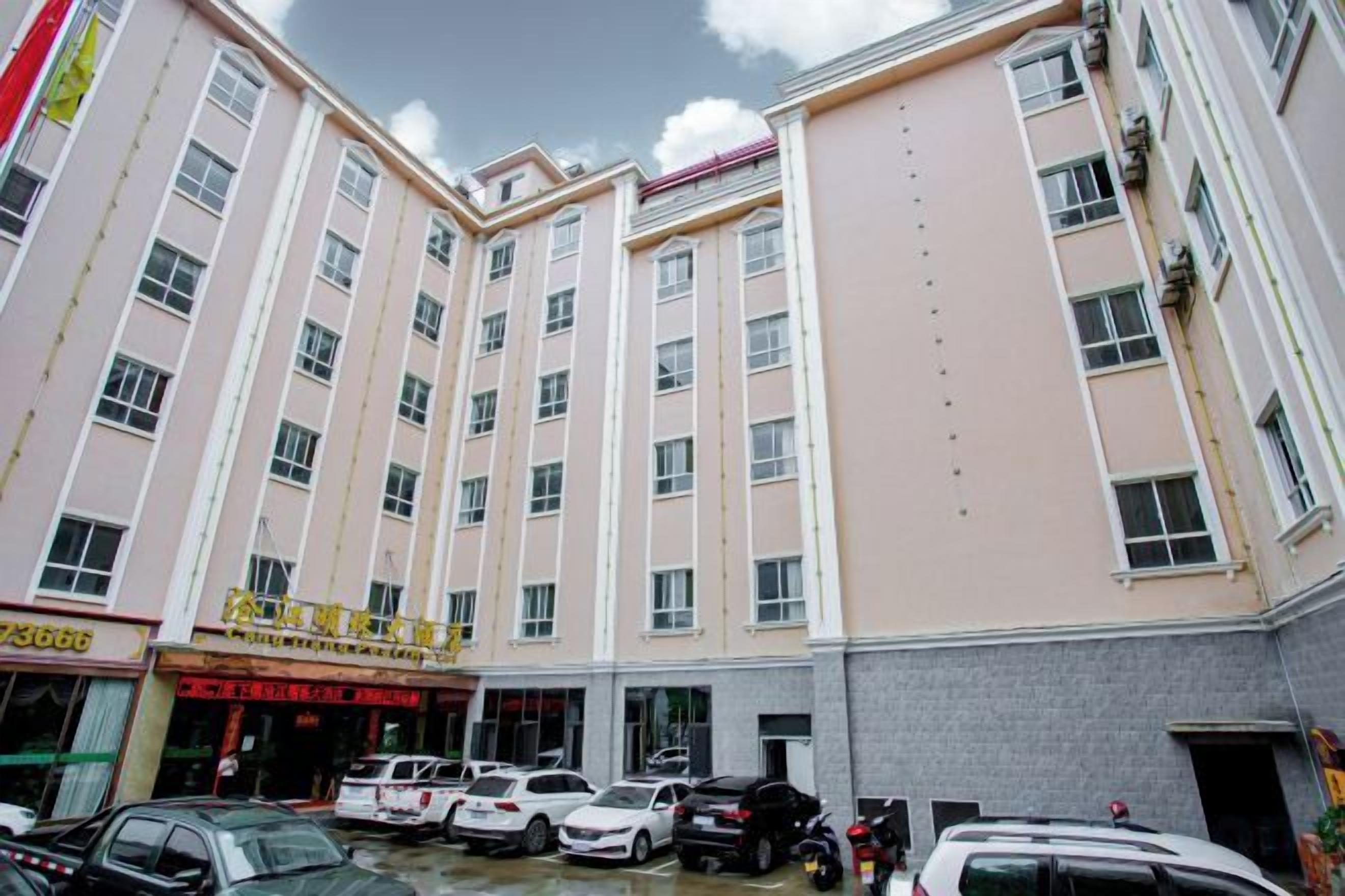 Un hotel de varios pisos con un patio central, varios coches estacionados y un cartel con texto.