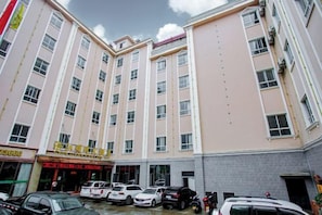 Un hôtel à plusieurs étages doté d’une cour intérieure, où sont garées plusieurs voitures, et d’une enseigne avec du texte.