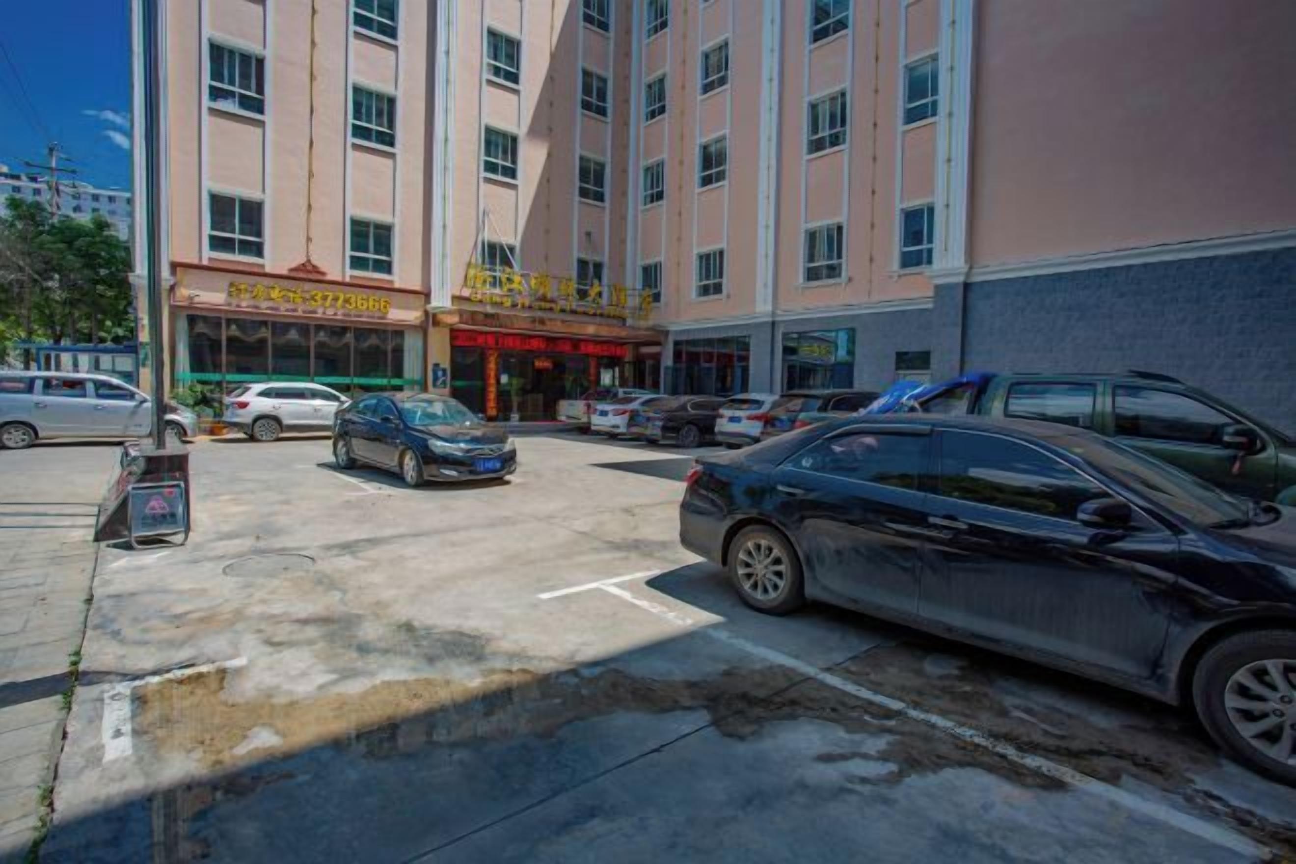 A multi-story hotel with a parking lot, several cars, and a storefront with signage.