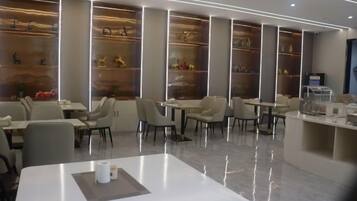 A modern restaurant with a clean, minimalist design, featuring white tables, comfortable seating, and decorative shelves with items.