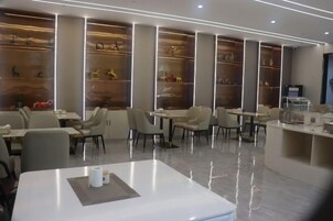 Un restaurante moderno con un diseño limpio y minimalista, con mesas blancas, asientos cómodos y estantes decorativos con objetos.