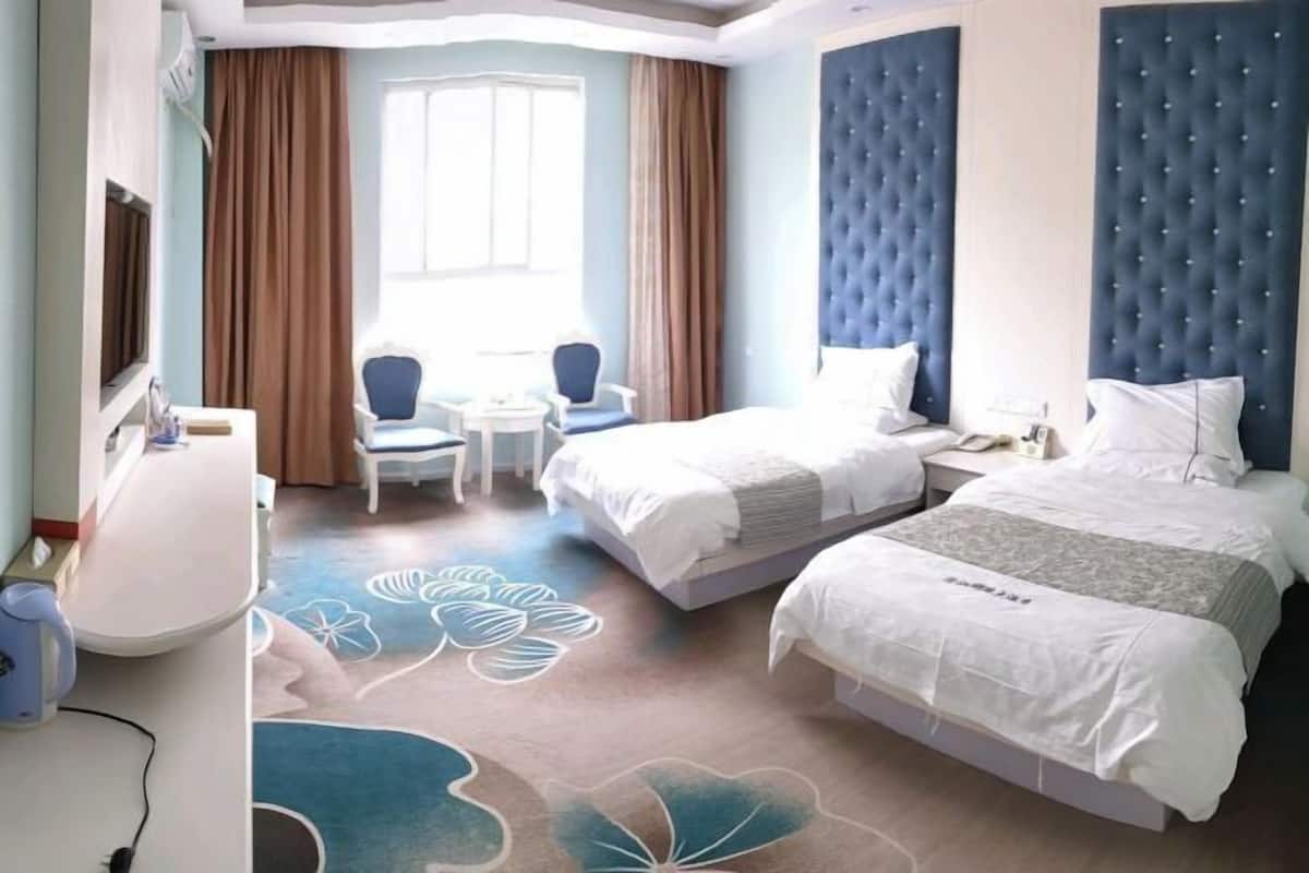 Hotellihuone, jossa on kaksi sänkyä, työpöytä, tuoli ja ikkuna, jossa on verhot.