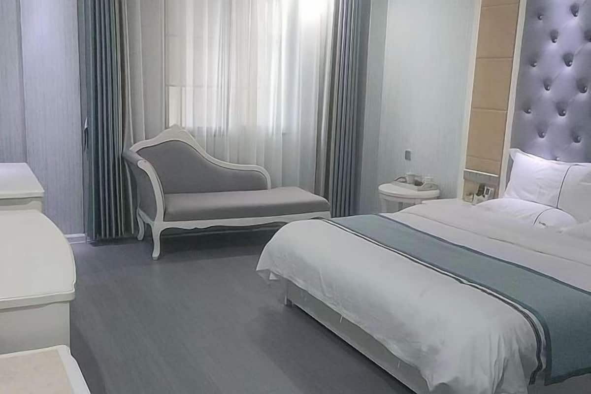 Moderni hotellihuone, jossa on suuri sänky, oleskelualue ja yöpöytä.