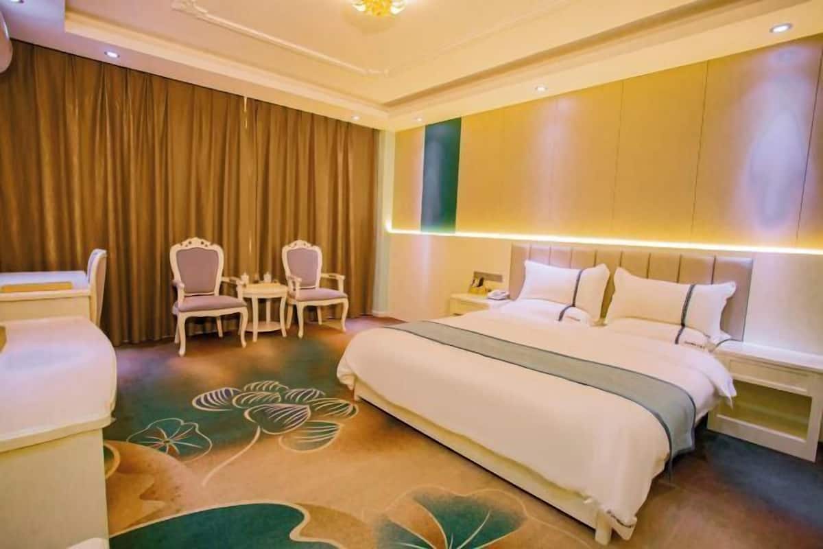 Hotellihuone, jossa on sänky, kaksi tuolia, pieni pöytä, yöpöytä ja verho.
