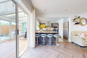 A modern kitchen with a central island, bar stools, and a dining area with chairs. - Charming 3-Bed Wimbledon Home with Garden Views, Parking & Great Location (London)