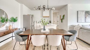 Une cuisine moderne avec des meubles blancs, un réfrigérateur en acier inoxydable et un coin repas comprenant une table en bois et deux chaises.
