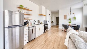 Une cuisine moderne dotée d’appareils électroménagers en acier inoxydable, d’étagères en bois et d’un coin repas avec une table et des chaises.