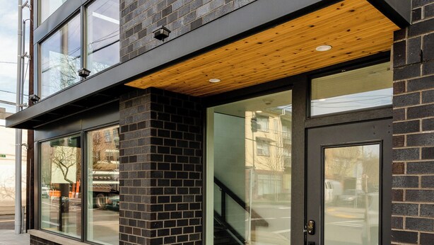 Un bâtiment moderne doté de grandes fenêtres, d’un plafond en bois et d’une façade en briques.