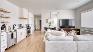 A modern kitchen with white cabinets, wooden shelves, and a dining area with a table and chairs. - Alberta Arts - 2BR - Walk to Food, Shops, & Art (Portland)