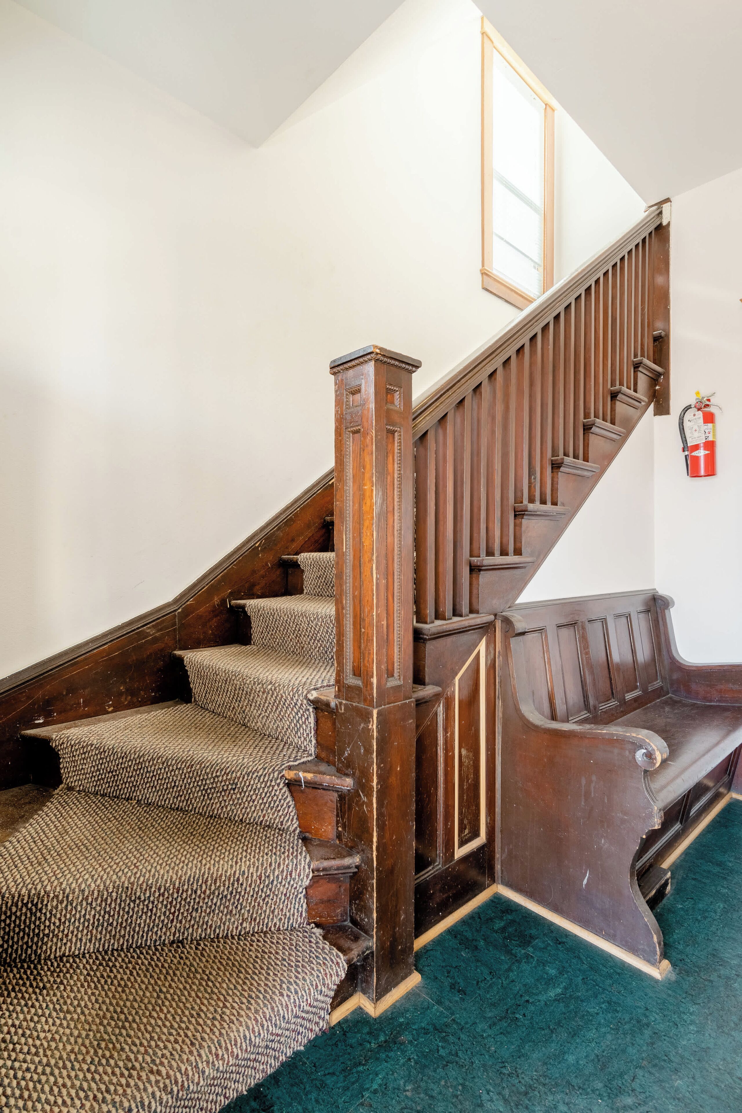A wooden staircase with a patterned carpet, a wooden handrail, and a fire extinguisher on the wall.