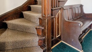 Una escalera de madera con alfombra estampada, barandilla de madera y un extintor en la pared.