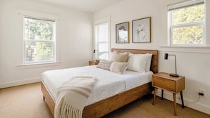 Un dormitorio con cama de madera, ropa de cama blanca, dos mesitas de noche y cuadros en la pared.