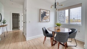 A modern dining area with a round table, four chairs, a chandelier, and a large window with a view of buildings. - Sleeps 12 - Exclusive Floor - Great for Groups (Portland)