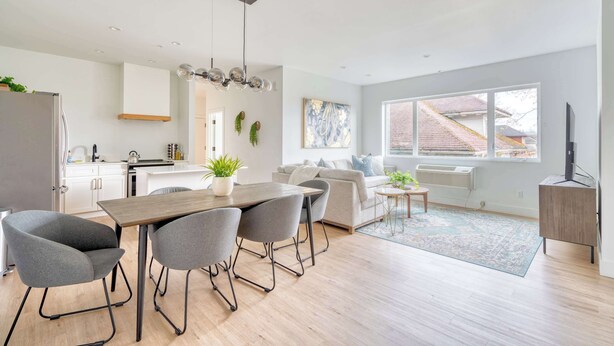 A modern living room with a sofa, a dining table with chairs, a kitchen area with a refrigerator, and a large window providing a view of the outside. - Sleeps 12 - Exclusive Floor - Great for Groups (Portland)