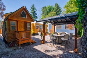 A wooden cabin with a porch and a covered patio area with a table and chairs. - The Timber Nook • Rustic Charm • Walkable Location (Portland)