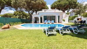 A poolside area with a swimming pool, lounge chairs, and a white building with green shutters.