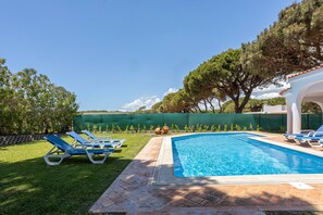 A swimming pool with blue water, surrounded by a tiled deck and a grassy area with blue lounge chairs. - Villa Moura by HelloVacations (Loulé)