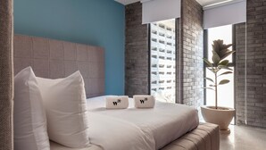 A modern bedroom with a large bed, a headboard, a potted plant, and a view of a building through a window. - Queretaro 77 by Wynwood House (Mexico City)