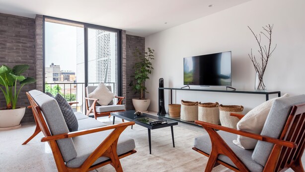 A modern living room with a large window, a flat-screen TV, and two wooden chairs. - Queretaro 77 by Wynwood House (Mexico City)