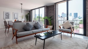 A modern living room with a grey sofa, a black coffee table, and a city view through large windows. - Queretaro 77 by Wynwood House (Mexico City)
