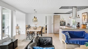 Ein modernes Wohnzimmer mit einem schwarzen Ledersofa, einem blauen Couchgarnitur und einem Essbereich mit Holztisch und Stühlen.